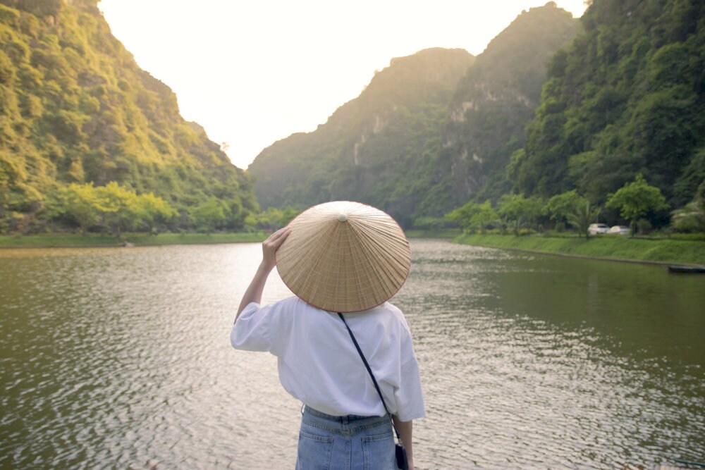 A serene moment as a girl in a traditional conical hat gazes across the tranquil lake